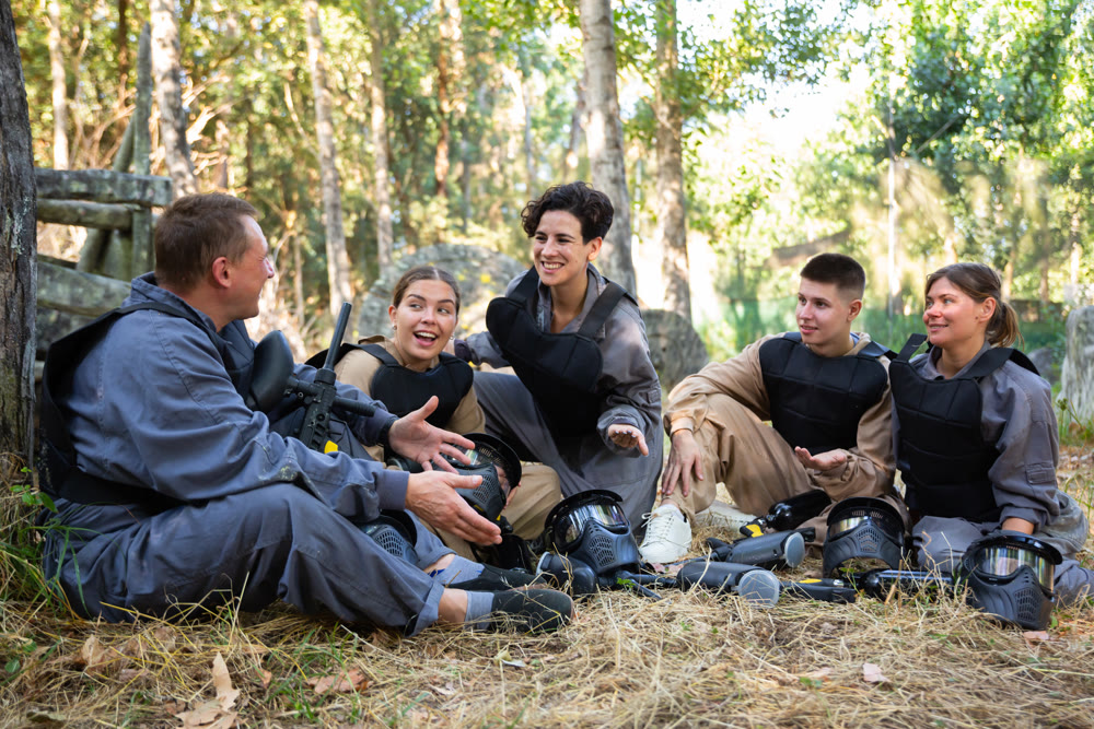 Positive paintball players sitting on battleground and chatting