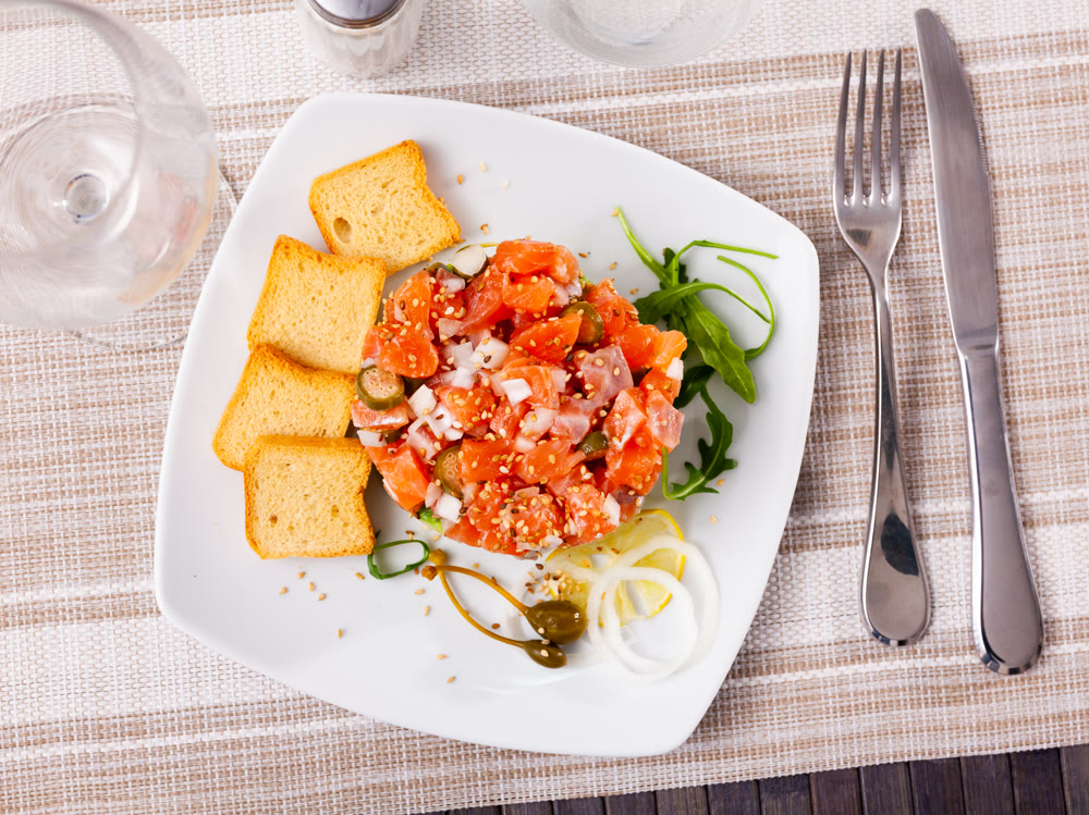 Salmon tartare with avocado garnished with capers, arugula, onion, lemon and toasts