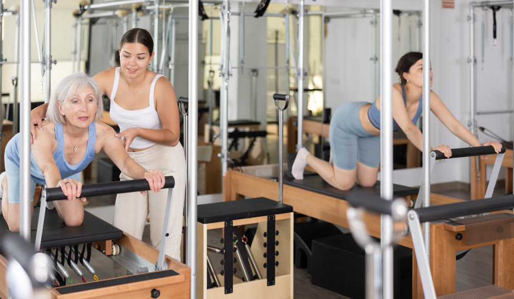 Elderly woman exercising on reformer with young female instructor