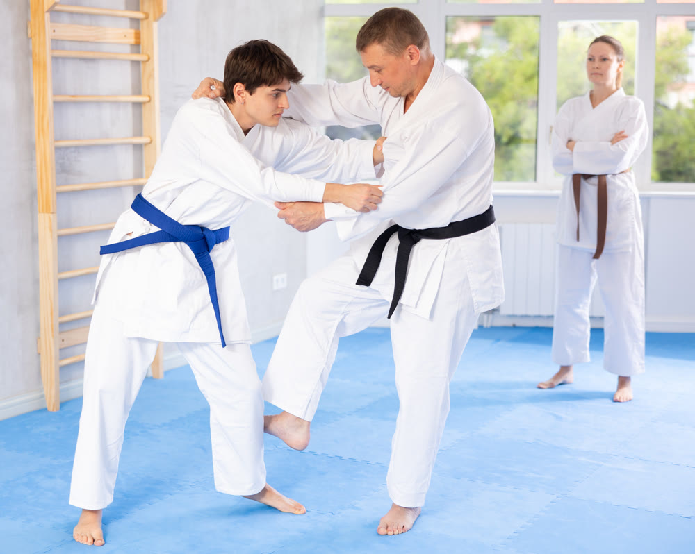 Two males practicing judo together on sports mats under the guidance of trainer
