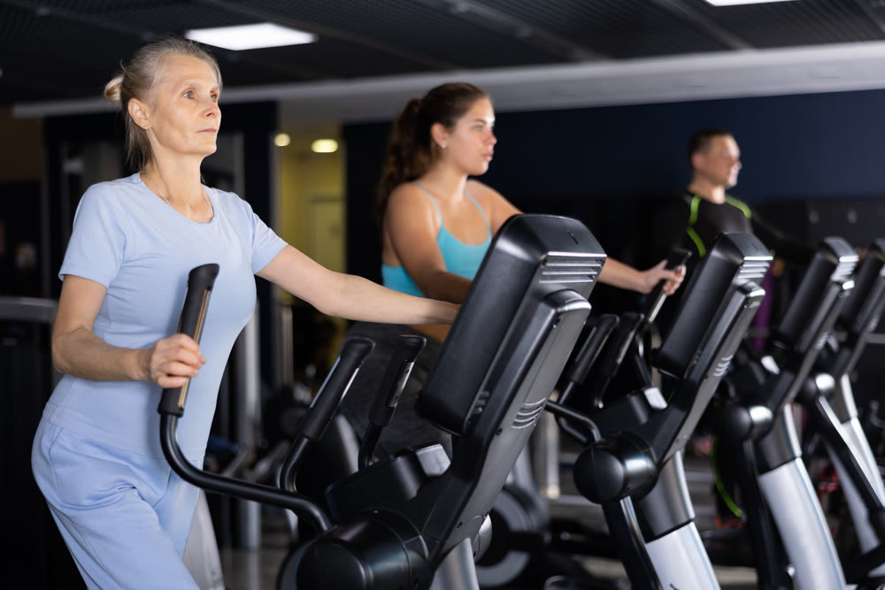 Sporty senior woman exercising on elliptical trainer in gym