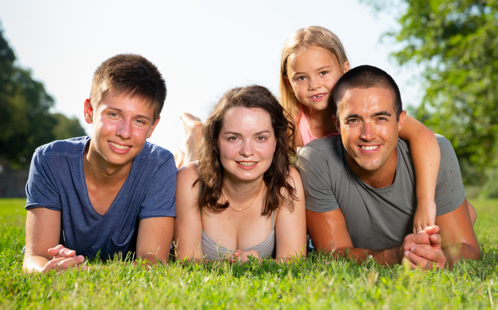Happy parents with two kids laying on grass in sunny summer park