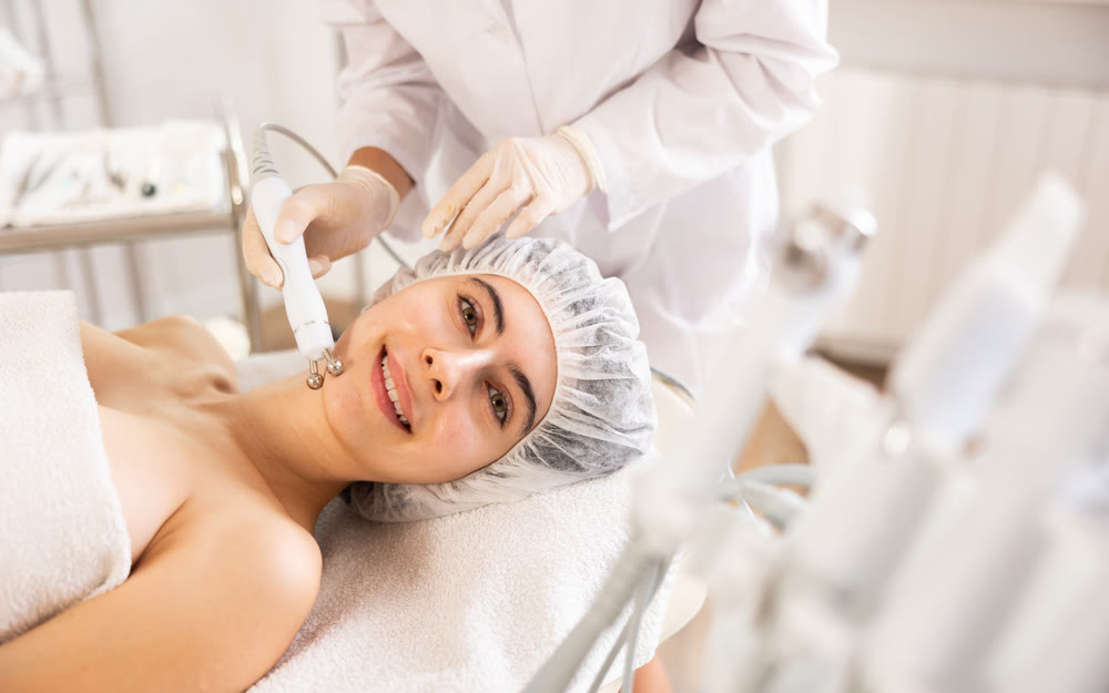Young woman cosmetologist doing microcurrent procedure to young woman