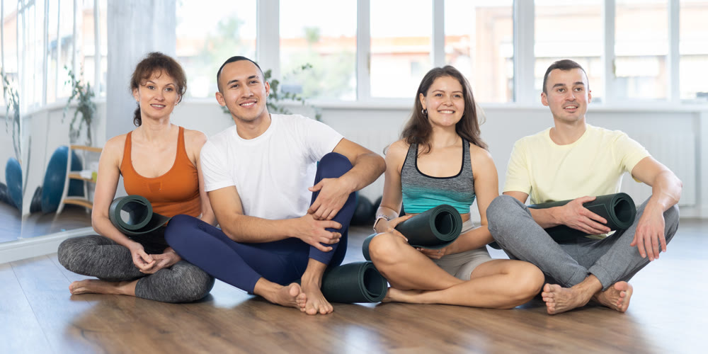 Portrait of athletic men and women with mats in hands about to practice yoga in gym