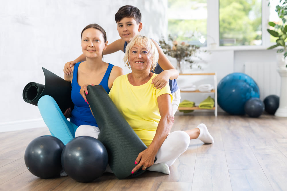 Three people of different ages engaged in yoga sitting on the floor in training room
