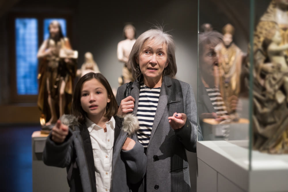 Elderly female tutor showing tween girl ancient sculptures in museum