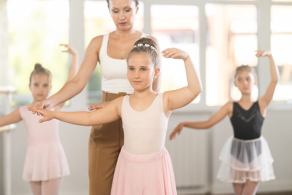 Girls in ballet class perform third position with correction of female mentor