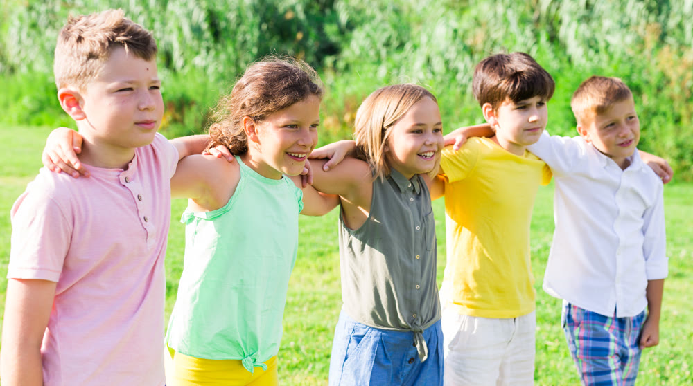 Portrait of five glad children who are walking and posing in park