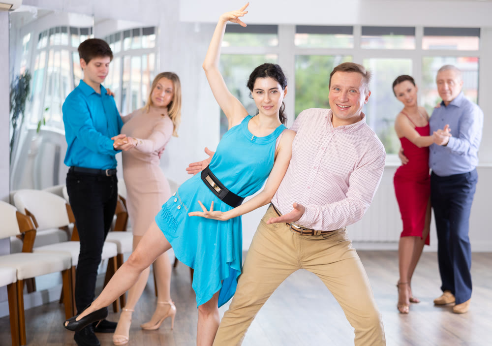 Men and women in festive clothes practicing tango dances in ballroom