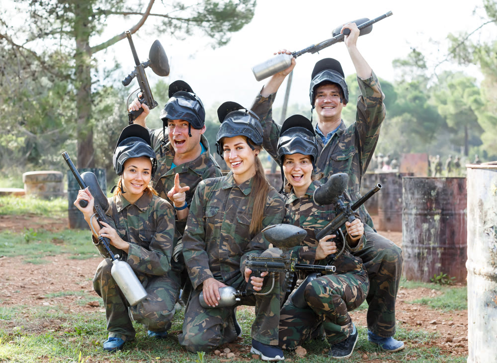 Portrait of positive team of paintball players with marker guns outdoors