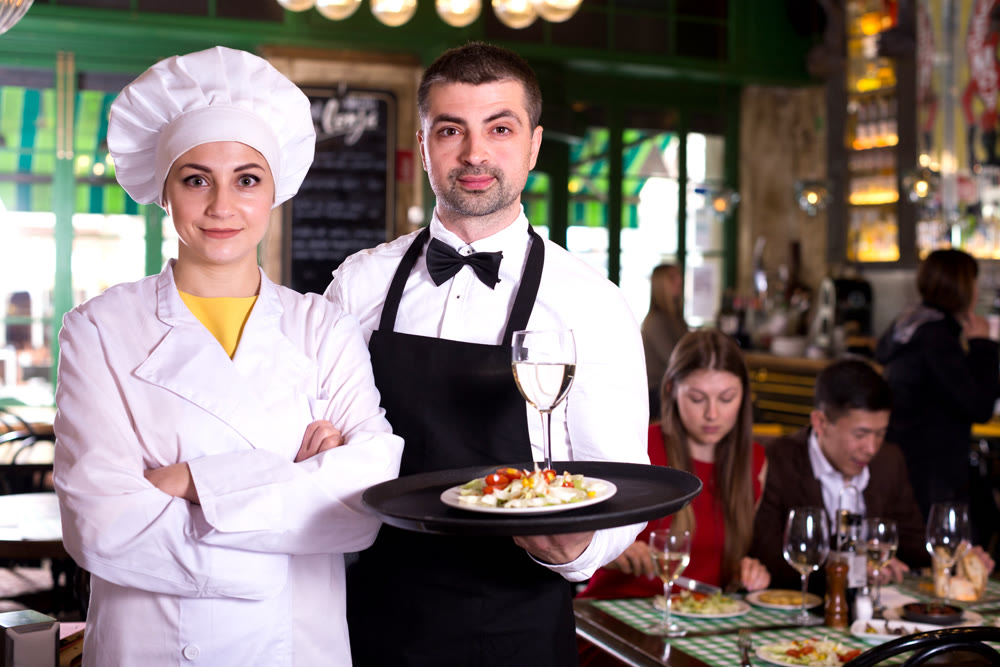 Man waiter and woman cook are standing with order for clients