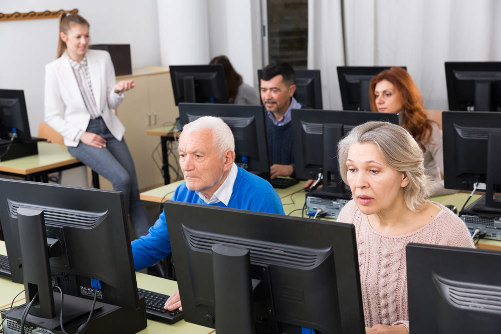 Elderly people working on computers with young teacher