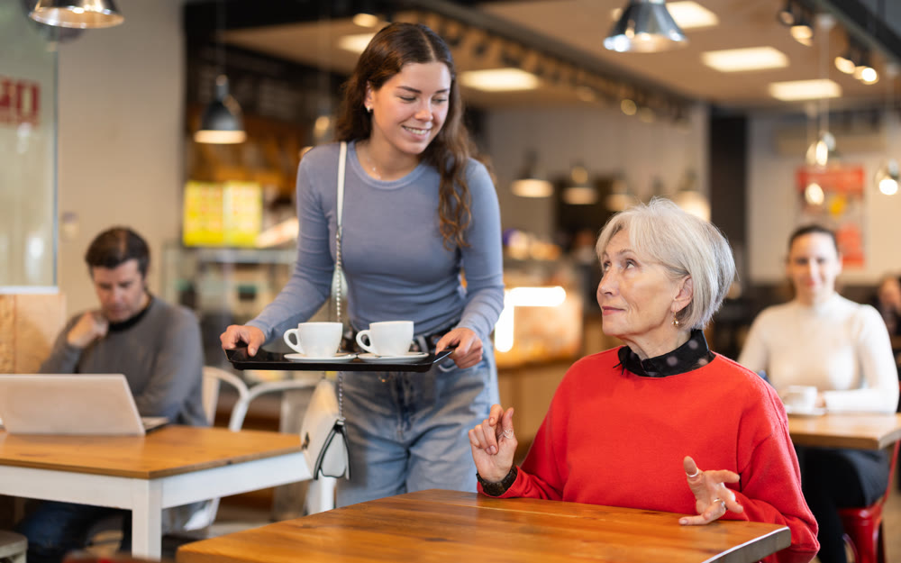 Adult daughter takes care of mature mother in cafe - brought tray with two cups of coffee