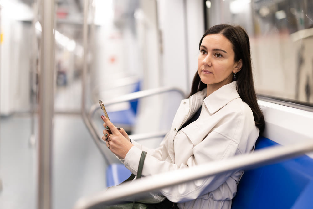 European woman sitting on seat in subway train and using smartphone