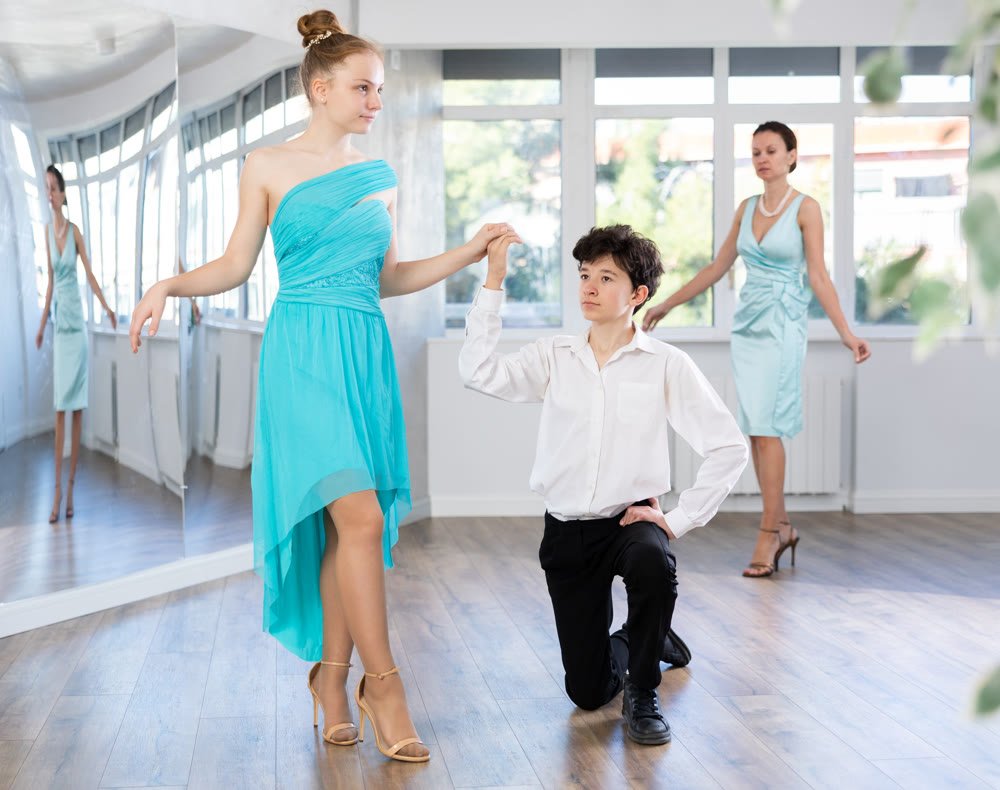 Girl stepping around boy standing on knee during dance rehearsal