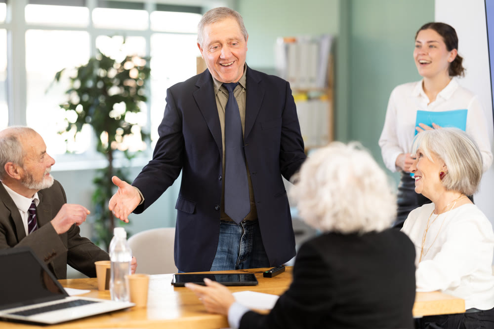Senior male speaker shares happy news, makes participants laugh