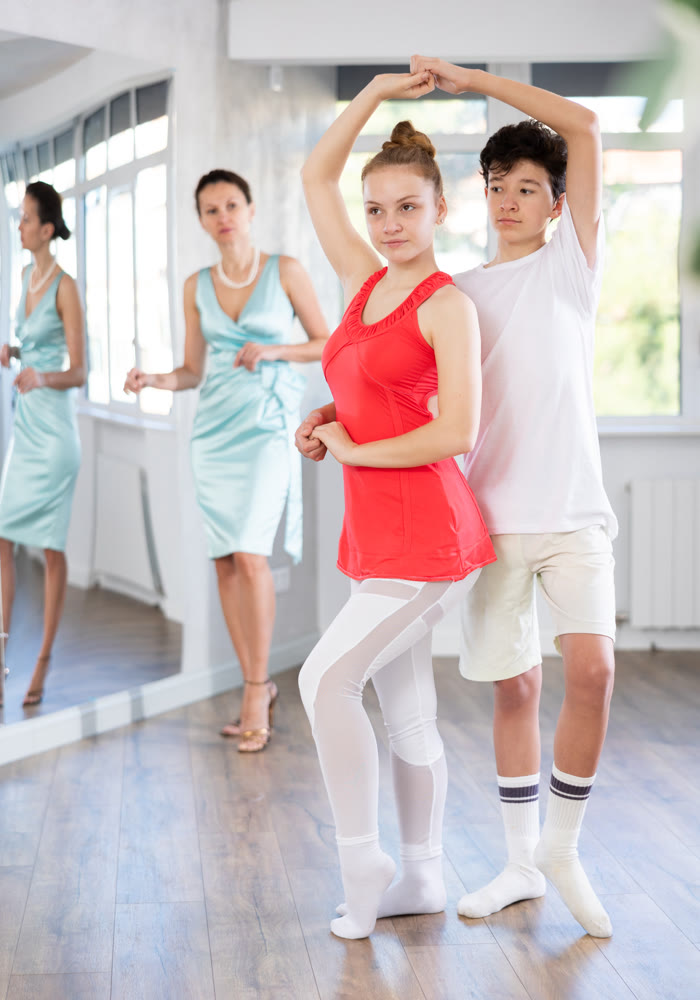 Experienced dance teacher teaching ballroom dancing to a couple of teenagers in studio