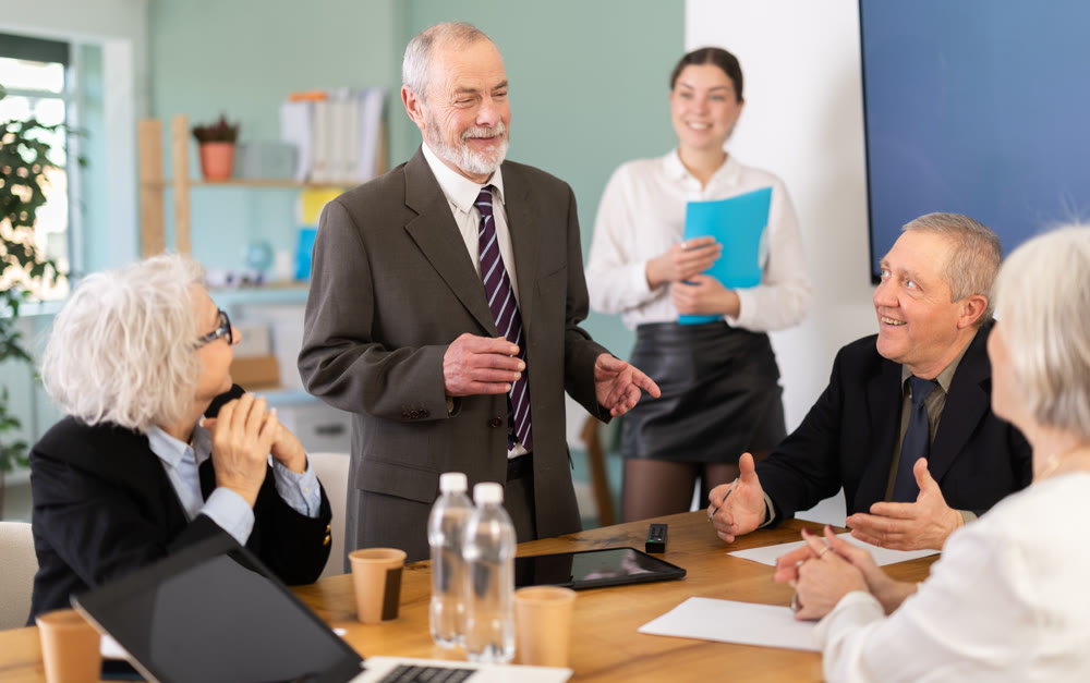 Senior male speaker shares happy news, makes participants laugh