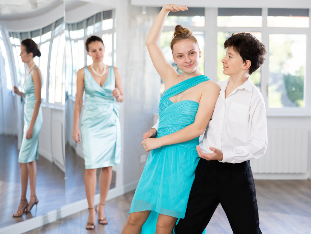 Teenage girl and boy practicing waltz in dance hall with female mentor