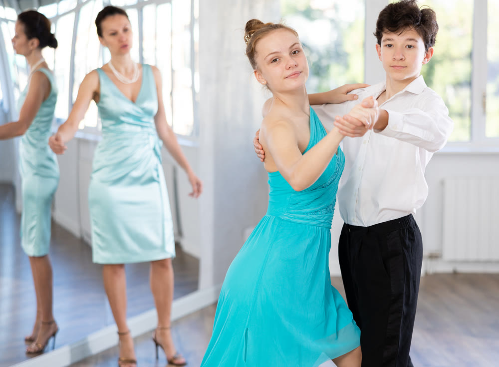 Girl and a boy in festive clothes learn to dance tango under guidance of teacher