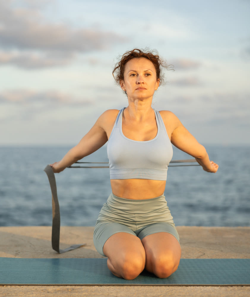 Atletic woman doing yoga with stretch band on seashore