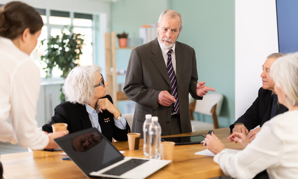 Male boss reprimanding upset subordinates sitting at table in office meeting room, expressing dissatisfaction with work