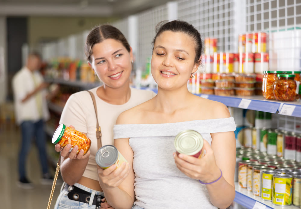 Two female shoppers choosing canned food in grocery store