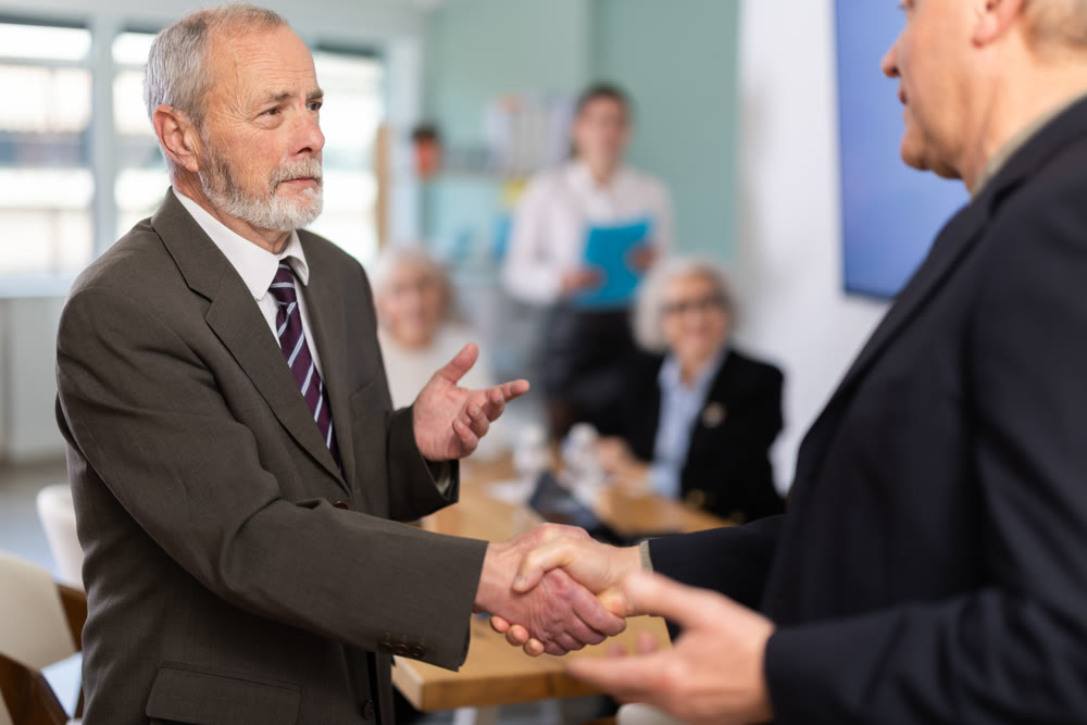 Senior men participants of meeting end business negotiations with handshake