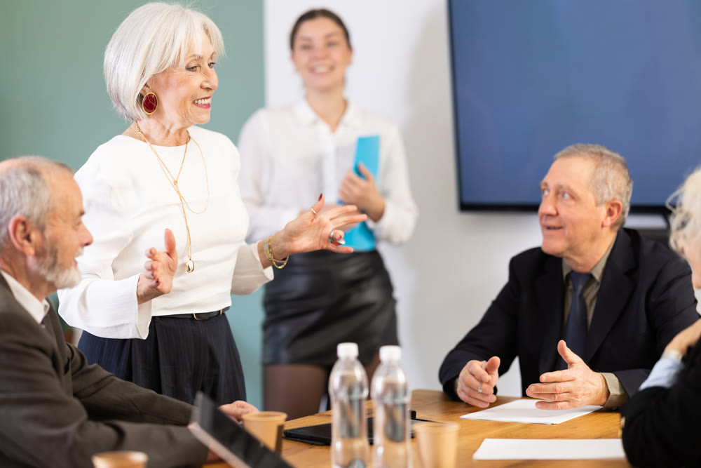 Elderly woman holds meeting while smiling colleagues listen