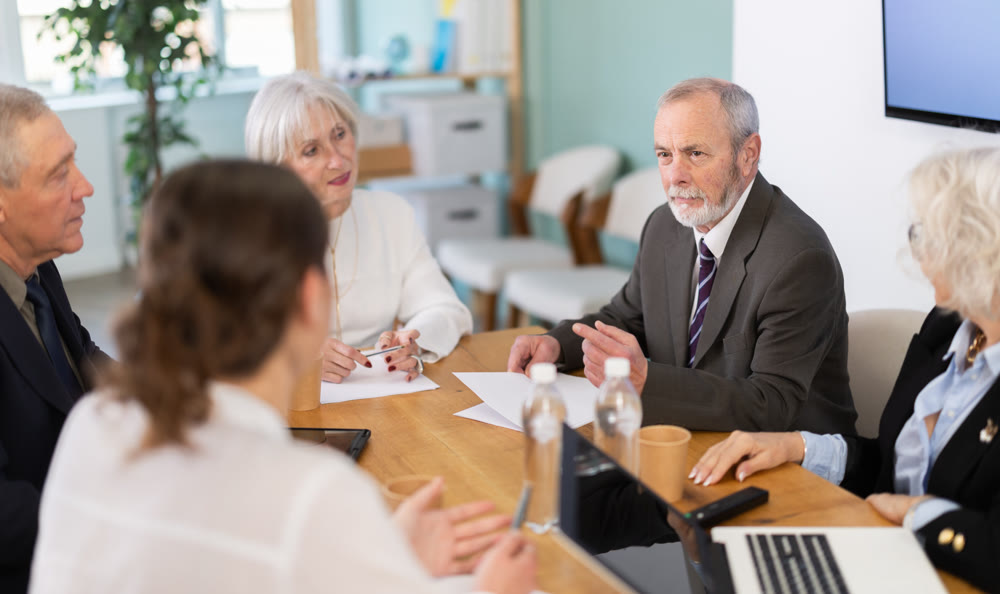 Elderly man leading meeting with senior colleagues at table