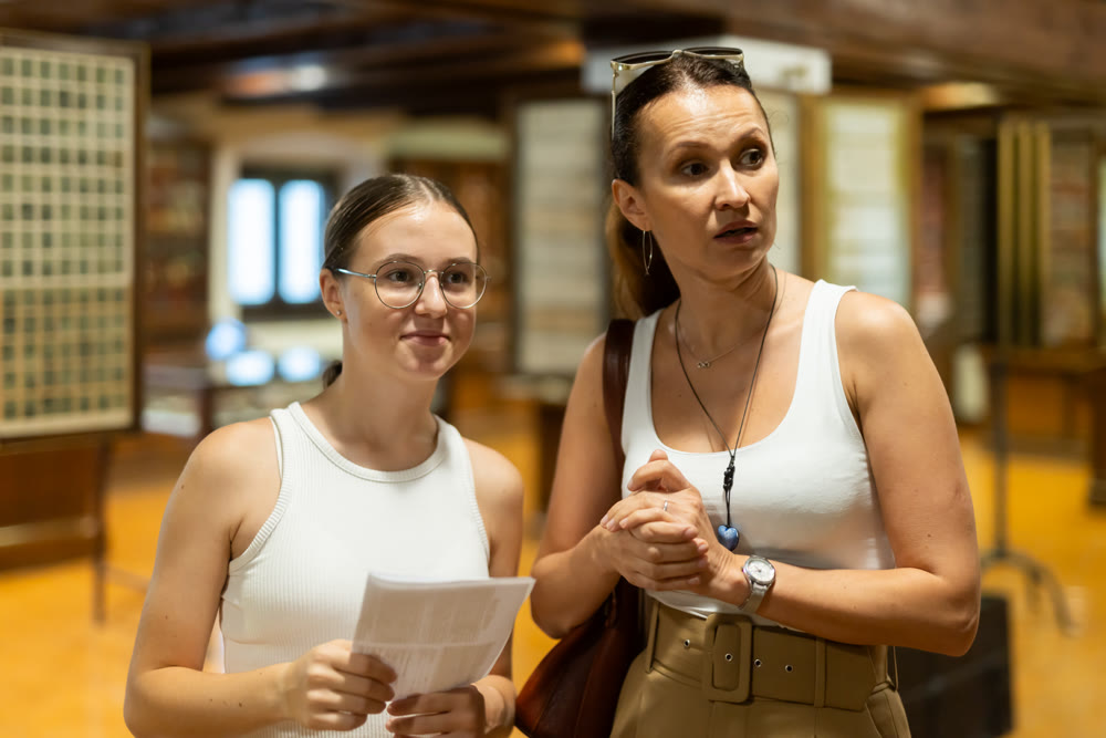 Young woman with teen daughter walk around museum, view antique appliances in museum hall