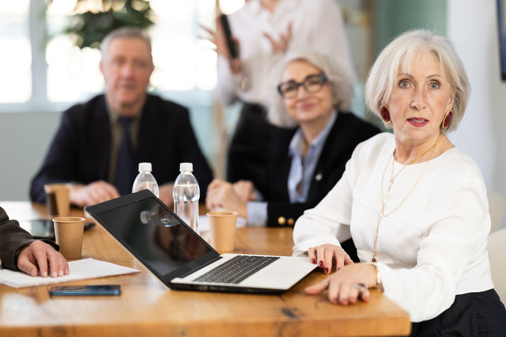 Office coworkers watching presentation while sitting at table with laptop, notes