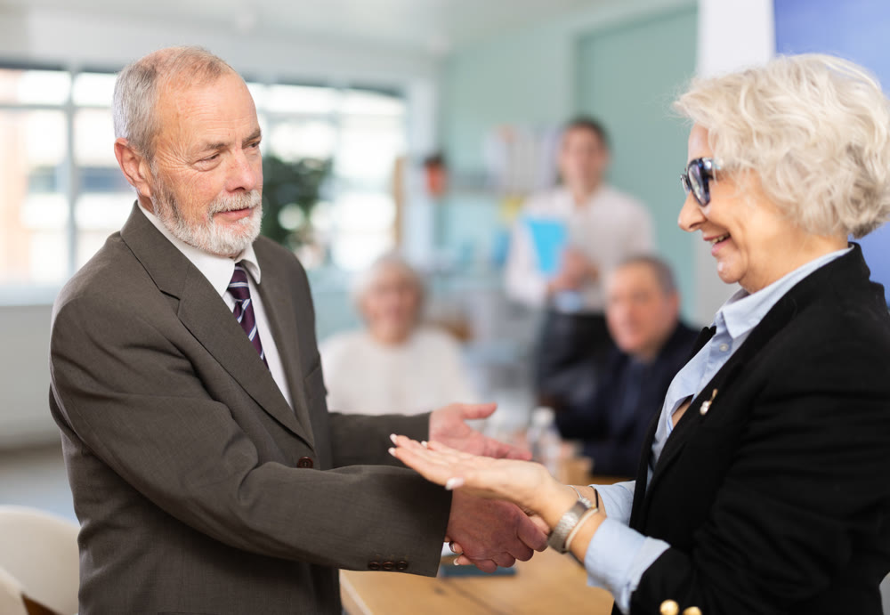 Senior male and female participants of meeting end business negotiations with handshake