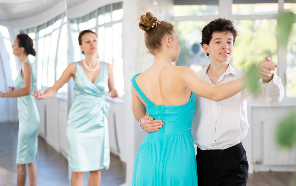Experienced female dancer teaches tango to pair of teenagers in ballroom