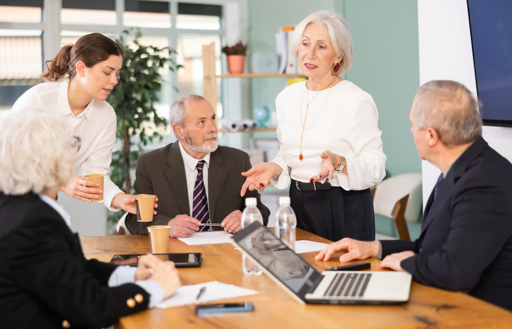 Elderly man leading meeting with senior colleagues at table