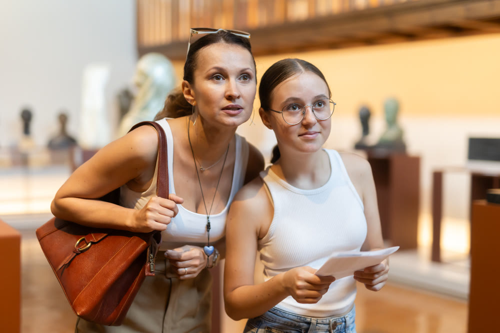 Young woman with teen daughter walk around museum, view sculpture in museum hall