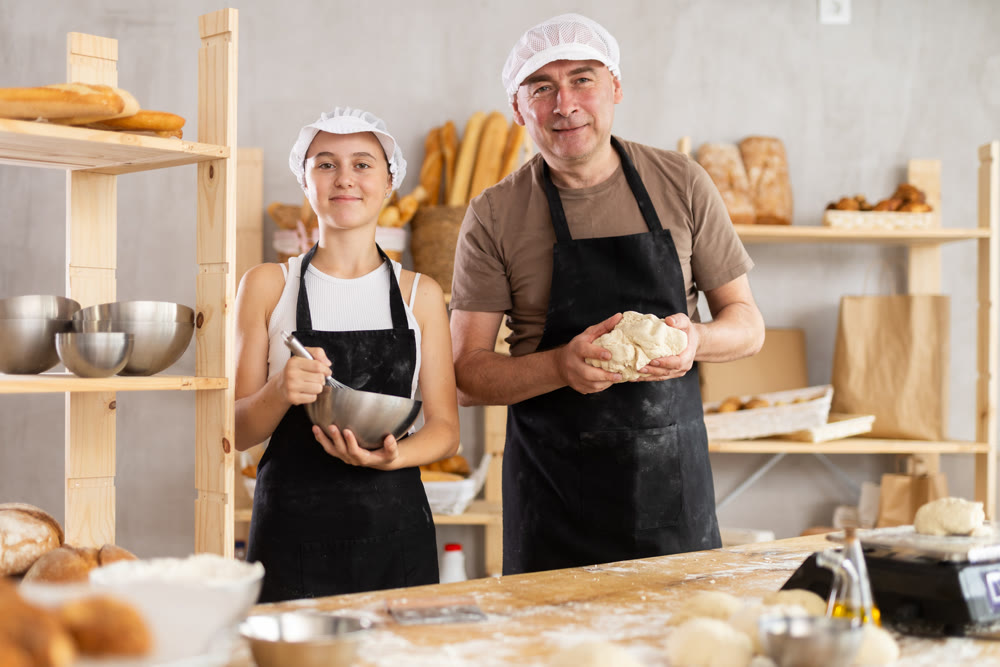 Male baker holding dough and teenage girl whipping in bowl