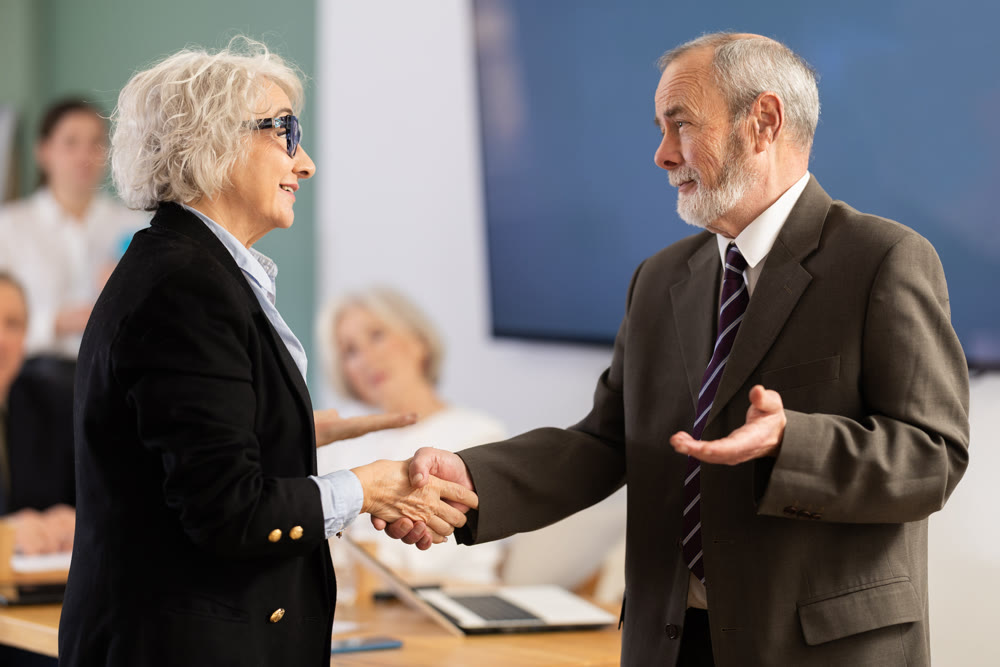 Senior male and female participants of meeting end business negotiations with handshake