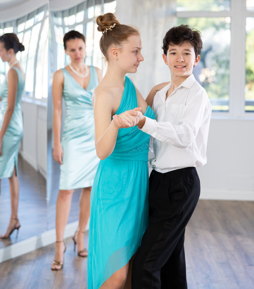 Girl and a boy in festive clothes learn to dance tango under guidance of teacher