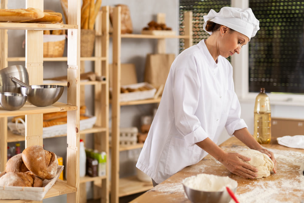 Woman works in bakery as baker, kneads dough, works with flour.