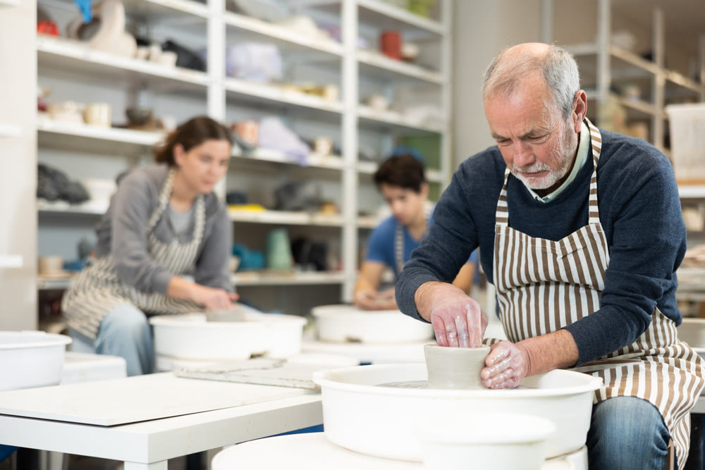 Elderly male potter works on potter wheel to create clay vase