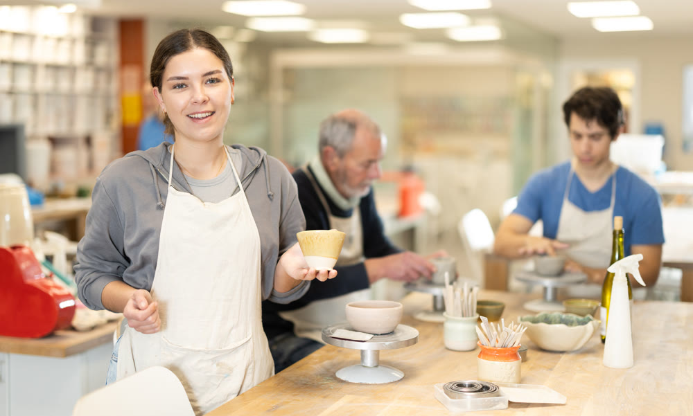 Smiling female potter demonstrates a clay cup he made with his own hands