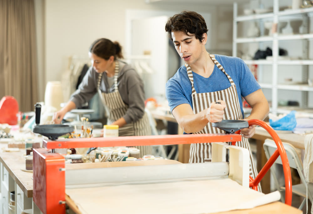 Young man rolling raw clay with mechanical slab roller