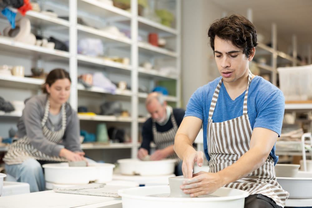 Young man shaping pottery on wheel in ceramics studio
