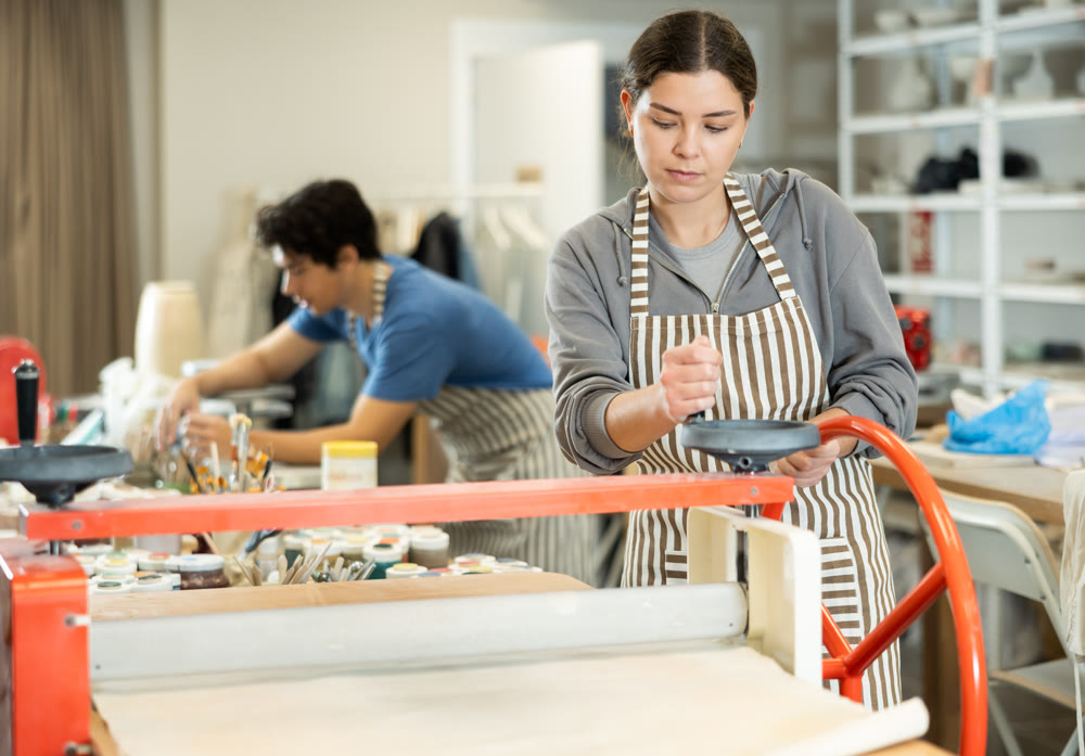 Young woman rolling raw clay with mechanical slab roller