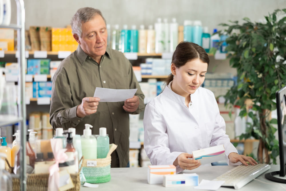 Woman employee at counter with computer sells pills and ointments to senior male customer