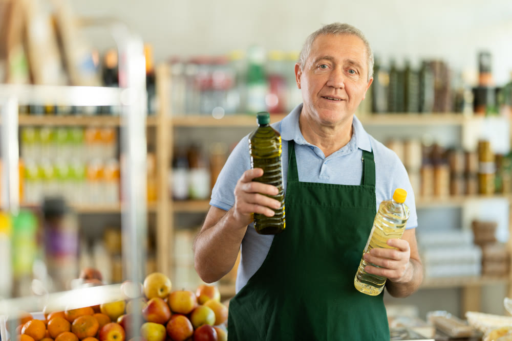 Elderly man seller offers vegetable oil in grocery store