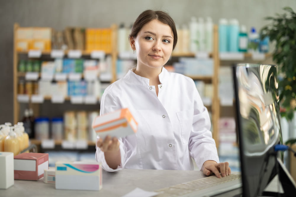 Female pharmacist standing at drugstore with medical product in hands