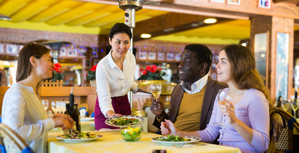 Asian waitress serving cheerful man and women over dinner in restaurant