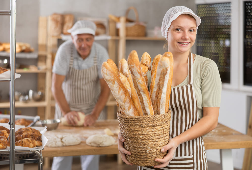 Smiling young female baker holding golden baguettes